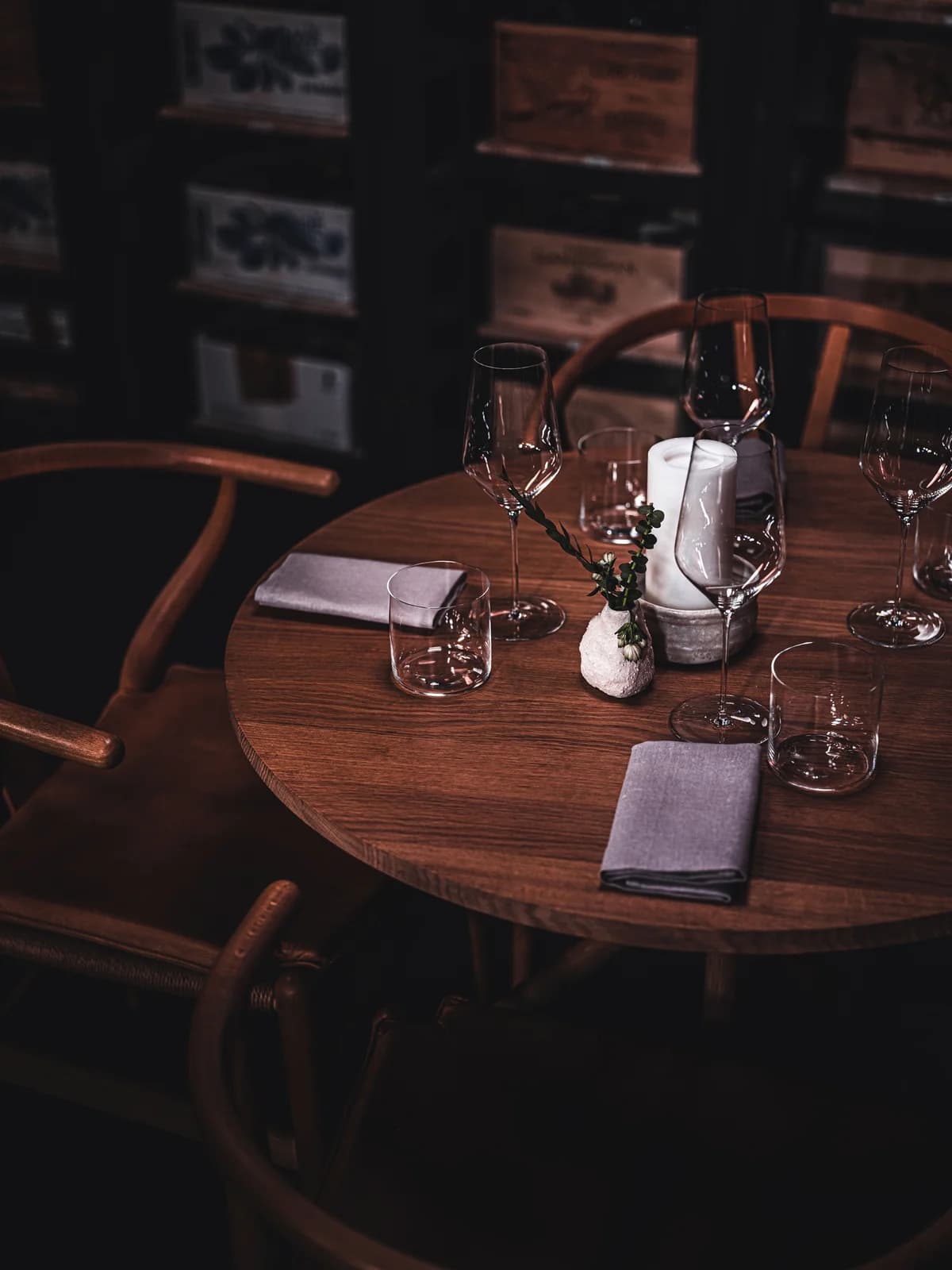 A round wooden table set with wine glasses, linen napkins, and flowers